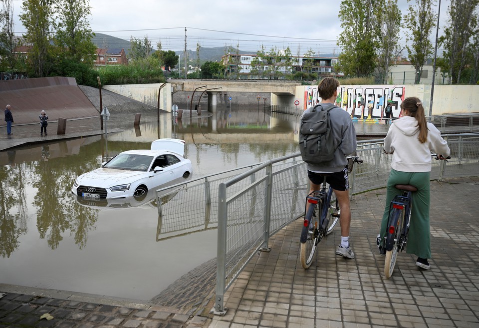 Ciclistas observam um carro inundado nos subrbios de Castelldefels, em Barcelona (Foto: Josep LAGO / AFP)