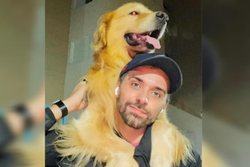 Homem branco com barba rala e bon azul segura cachorro Golden Retriever nos ombros