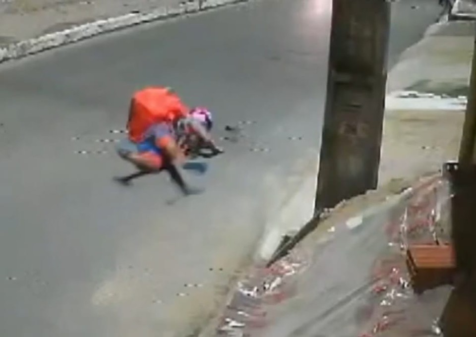 As imagens mostram o entregador tentando fugir, ao mesmo tempo que um dos criminosos, com a arma em punho, chuta a moto dele, derrubando o veculo, e atira, atingido a mochila (Foto: Reproduo)