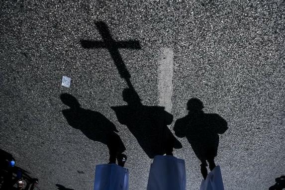 FOTOS DO DIA  (Sombra de meninos do altar carregando um crucifixo  vista na rua enquanto pessoas participam da Festa de Deus (Precesso da Fte Dieu) para celebrar a celebrao de Corpus Christi, em Porto Prncipe, em 20 de junho de 2019. Foto de CHANDAN KHANNA / AFP.)