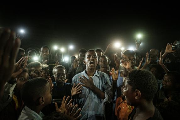 FOTOS DA SEMANA (As pessoas cantam slogans quando jovem recita um poema sobre revoluo, iluminado por telefones celulares, antes do dilogo direto da oposio com pessoas em Cartum em 19 de junho de 2019. Foto: Yasuyoshi CHIBA / AFP)