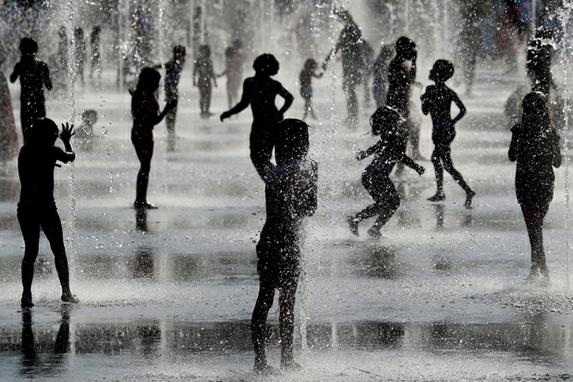 FOTOS DO DIA (Crianas brincam debaixo de jatos de gua em uma fonte enquanto se refrescam durante uma onda de calor em Nice em 26 de junho de 2019. (Foto de VALERY HACHE / AFP).)