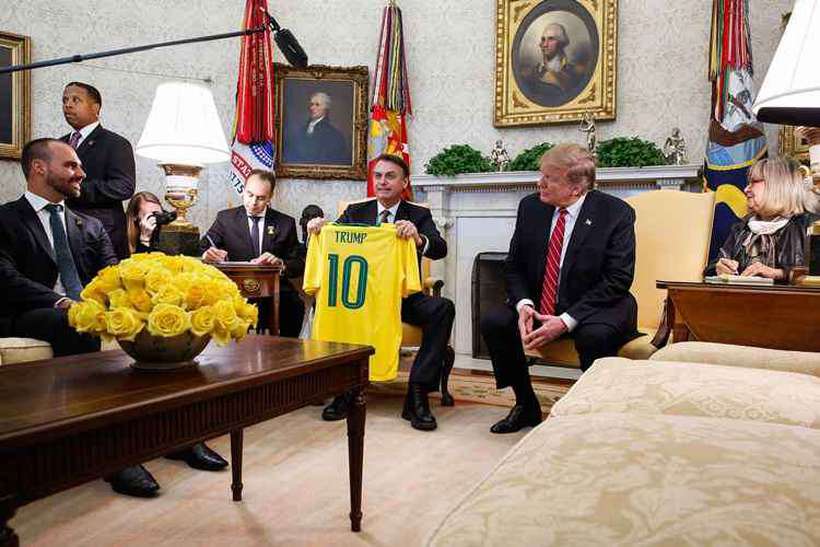 Eduardo Bolsonaro, sorri enquanto o pai mostra camisa ofertada a Trump. Foto: Isac Nbrega/PR