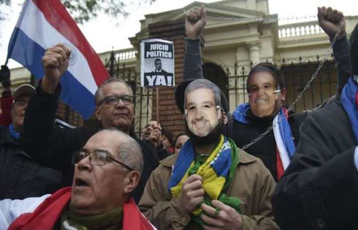 Ativistas com as bandeiras do Paraguai e do Brasil, e com mscaras de Mario Abdo Bentez, protestam contra o presidente: falam de traio  Ptria. Foto: Norberto Duarte/AFP.