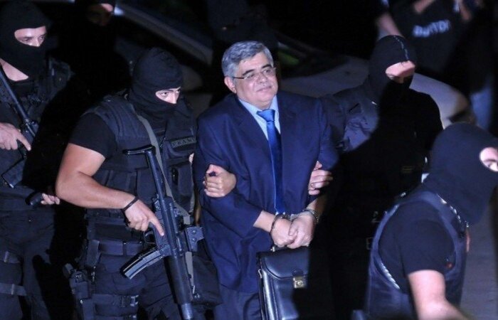 Golden Dawn Nikos Michaloliakos, líder do partido neonazista grego, é escoltado por uma polícia mascarada a um tribunal de Atenas. Registro de 2013 (Foto: Louisa Gouliamaki/AFP) Golden Dawn Nikos Michaloliakos, líder do partido neonazista grego, é escoltado por uma polícia mascarada a um tribunal de Atenas. Registro de 2013 (Foto: Louisa Gouliamaki/AFP)