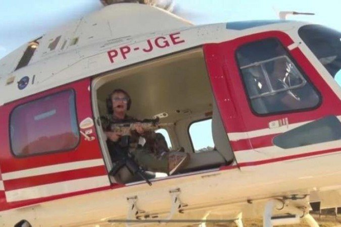 (Vídeo feito por Magda Moffato, que segura rifle e embarca em helicóptero atrás do foragido, foi considerado deboche contra policiais. Foragido é buscado por mais de 200 soldados. Foto: Reprodução/Facebook
) (Vídeo feito por Magda Moffato, que segura rifle e embarca em helicóptero atrás do foragido, foi considerado deboche contra policiais. Foragido é buscado por mais de 200 soldados. Foto: Reprodução/Facebook
)