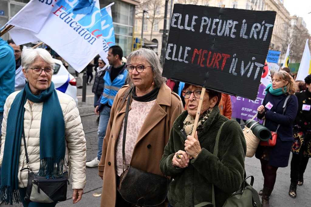 No protesto, mulher levanta um cartaz que diz: "Ela chora, ele ri, ela morre, ele vive" (Foto: Nicolas TUCAT / AFP)
